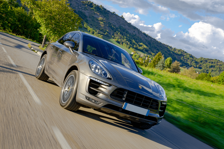 Grauer Porsche Macan auf Landstraße in grüner Landschaft