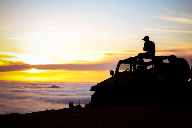 Jeep auf Berg über den Wolken beim Sonnenaufgang